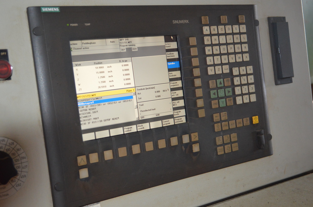 A Siemens Sinumerik control panel with a lit screen showing axis positions and a running program, mounted on the side of a beam line machine.